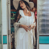 Soul Sister since 1969 long white dress on beautiful woman with a fringe shawl and retro floppy hat standing in a vintage trailer