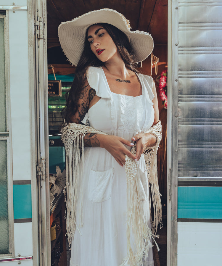 Soul Sister since 1969 long white dress on beautiful woman with a fringe shawl and retro floppy hat standing in a vintage trailer