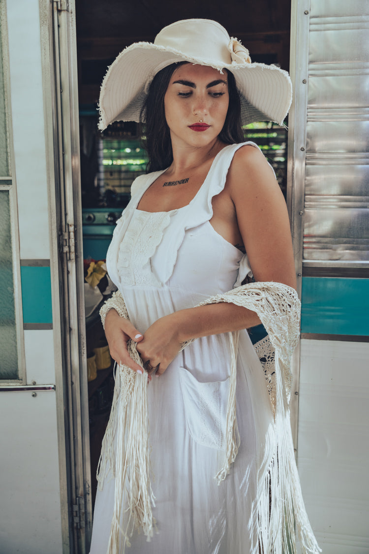 Soul Sister since 1969 long white dress on beautiful woman with a fringe shawl and retro floppy hat standing in a vintage trailer