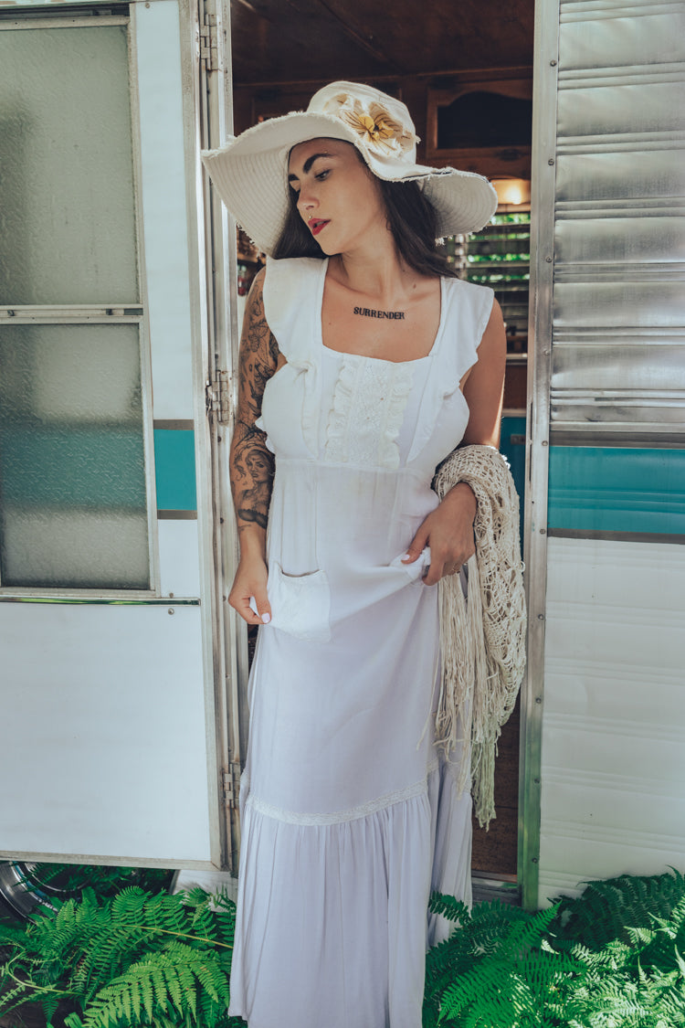 Soul Sister since 1969 long white dress on beautiful woman with a fringe shawl and retro floppy hat standing in a vintage trailer