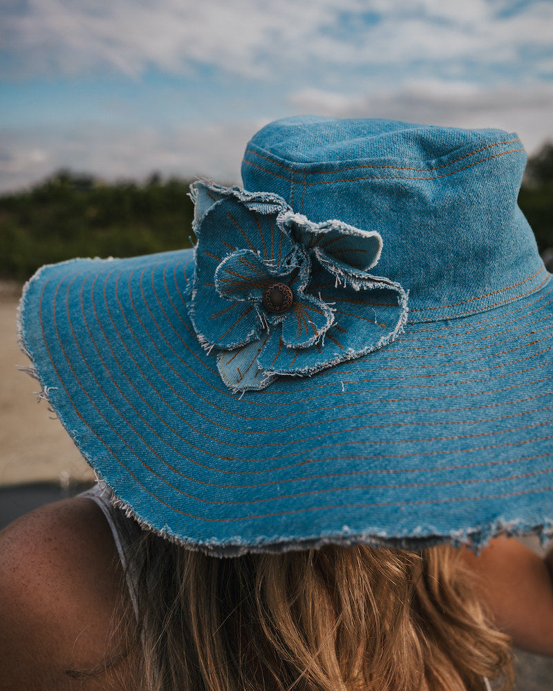 Blue denim sun hat with a flower detail against a blurred natural background Wearing Soul Sister since 1969
