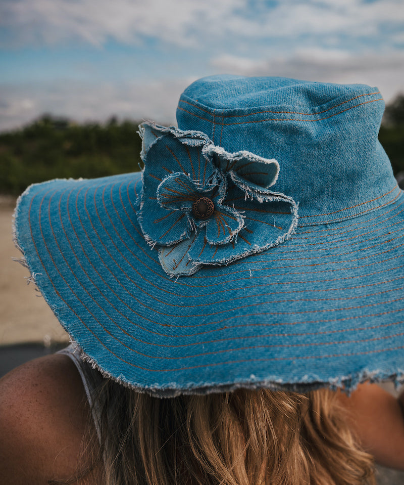Blue denim sun hat with a flower detail against a blurred natural background Wearing Soul Sister since 1969