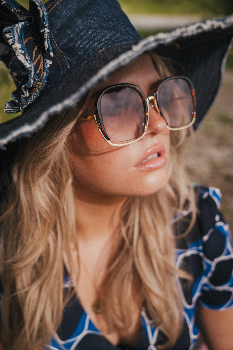 Woman wearing a black witch hat and sunglasses with a blurred natural background wearing Soul Sister since 1969.