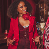 Woman in a red jacket and dark outfit with a floral top, standing in a bar setting.