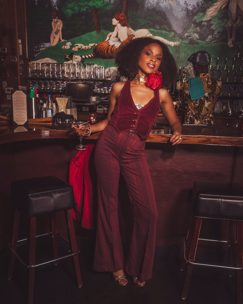 Woman in a burgundy outfit standing behind a bar with a vintage decor.