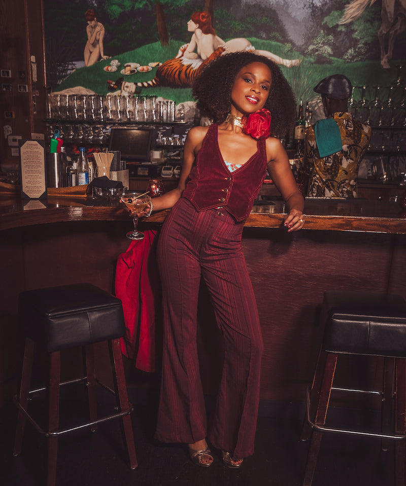 Woman in a burgundy outfit standing behind a bar with a vintage decor.