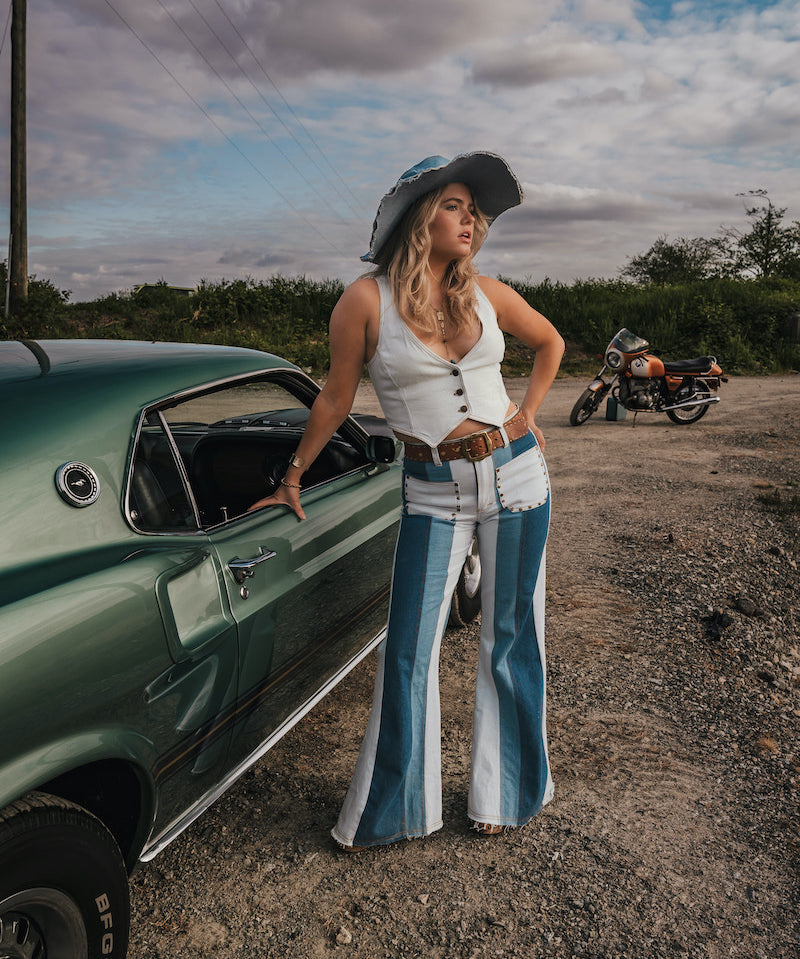 Woman in a vintage outfit standing next to a green car with a motorcycle in the background wearing Soul Sister since 1969.