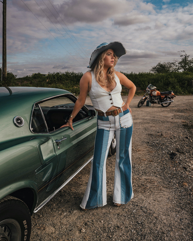 Woman in a vintage outfit standing next to a green car with a motorcycle in the background Wearing Soul Sister since 1969.