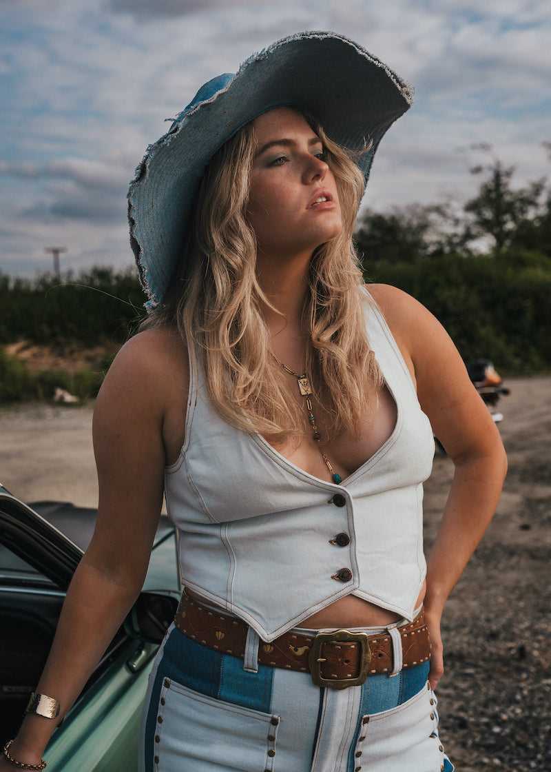 Woman in a white top and blue jeans with a cowboy hat standing next to a car outdoors wearing Soul Sister since 1969..