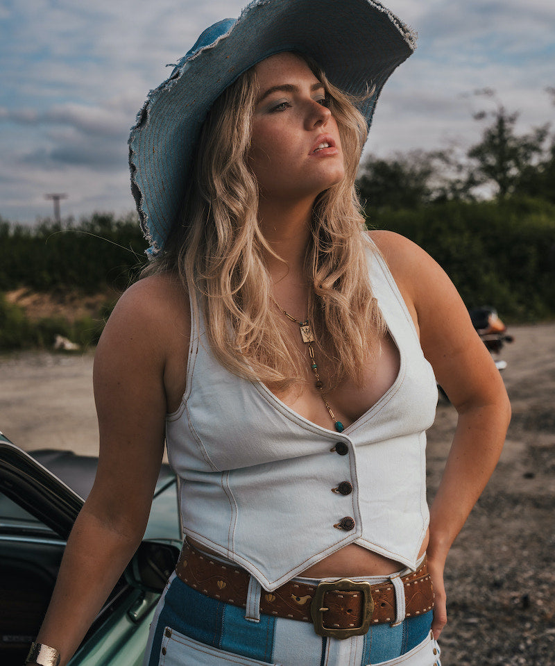 Woman in a white top and blue jeans with a cowboy hat standing next to a car outdoors wearing Soul Sister since 1969..