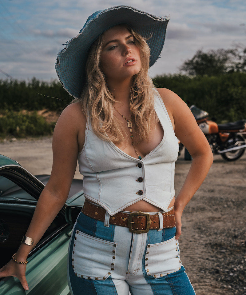 Woman in a white top and blue jeans standing next to a green car with a motorcycle in the background wearing Soul Sister since 1969.