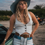 Woman in a white top and blue jeans standing next to a green car with a motorcycle in the background. Wearing Soul Sister since 1969