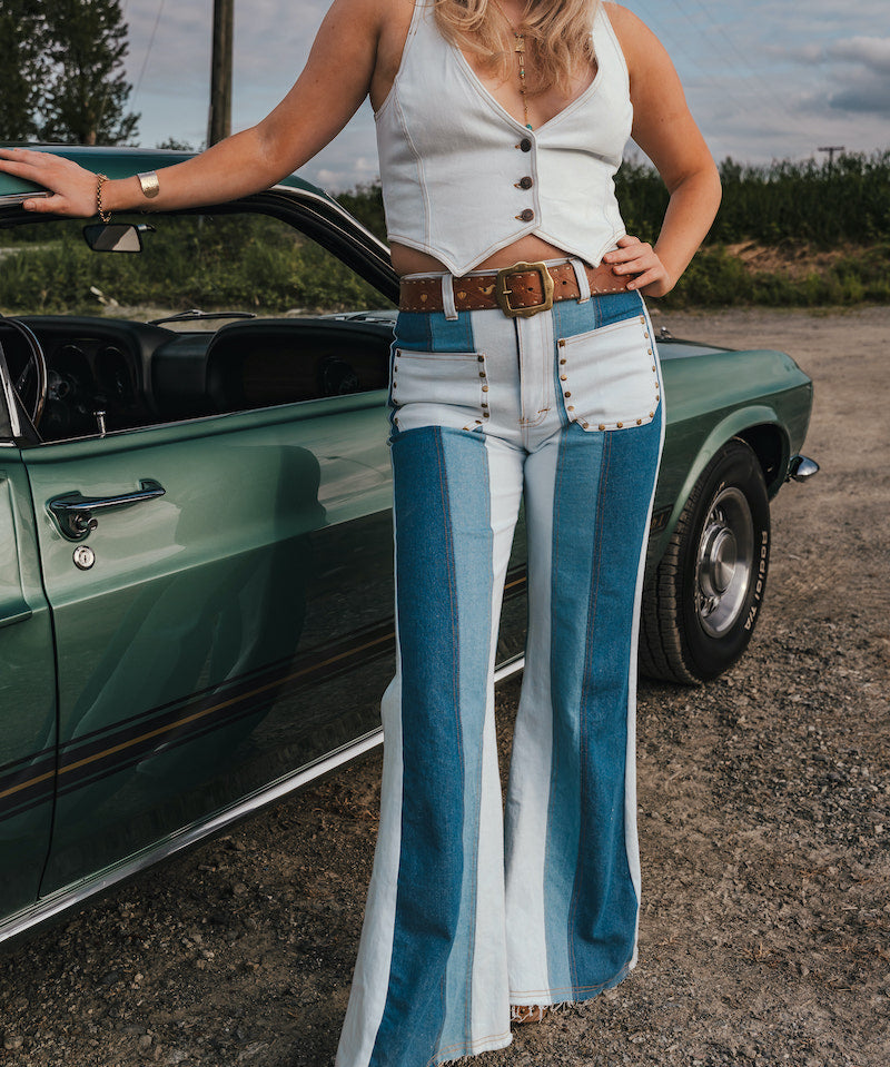 Woman in a white sleeveless top and blue bell-bottom pants standing next to a green classic car wearing Soul Sister since 1969..