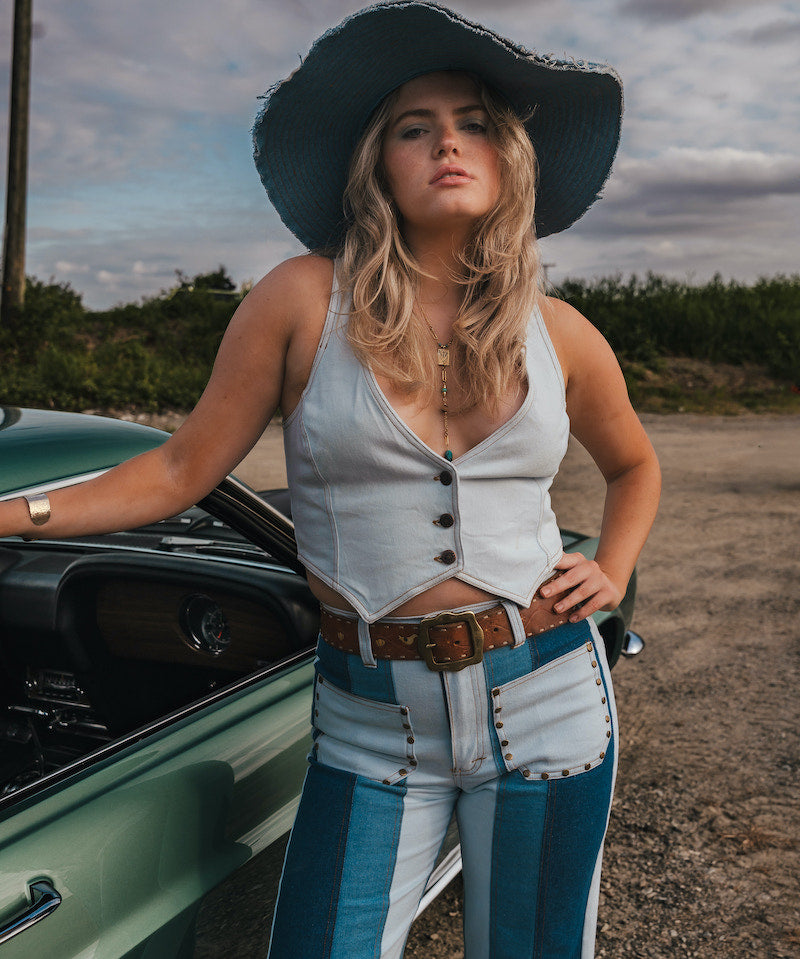Woman in a white top and blue jeans standing next to a green car on a dirt road wearing Soul Sister since 1969..