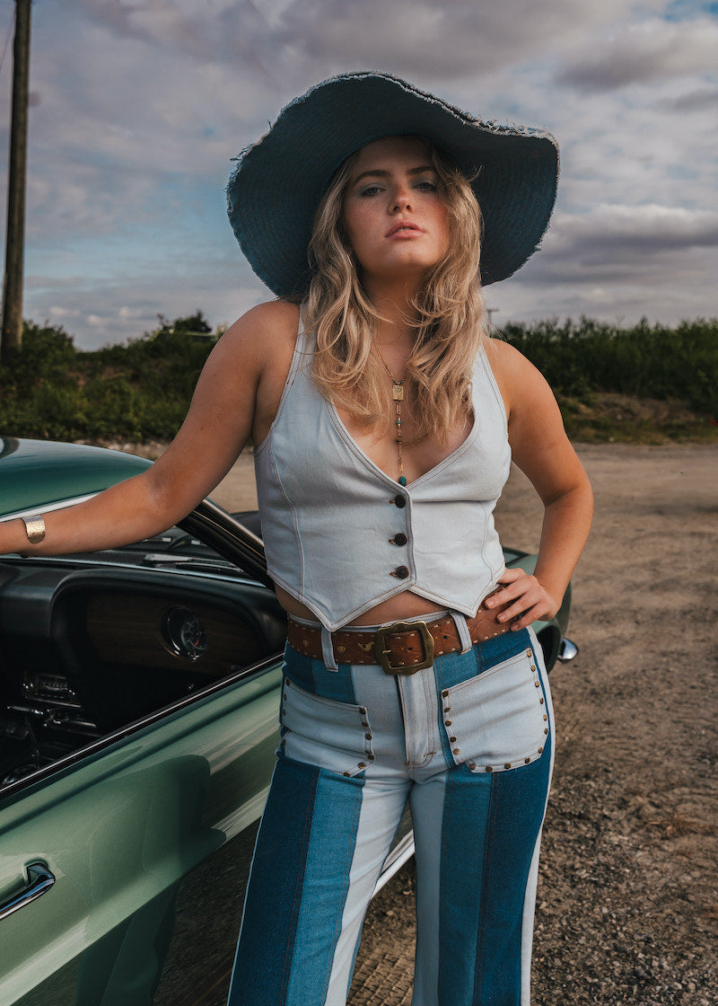 Woman in a white top and blue jeans standing next to a green car on a dirt road Wearing Soul Sister since 1969.