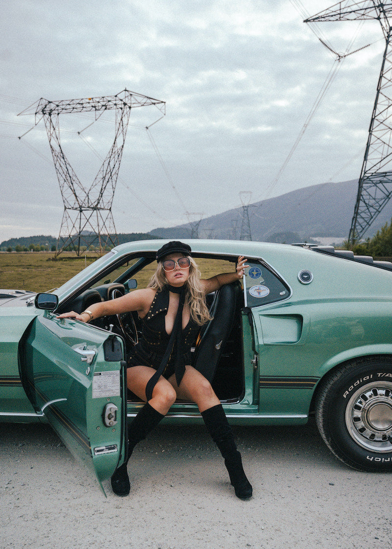 Woman leaning against a green car with power lines and mountains in the background wearing Soul Sister since 1969