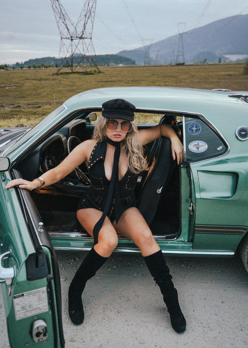 Woman in a stylish outfit sitting in an open car door with a scenic background wearing Soul Sister since 1969