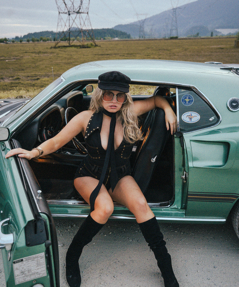 Woman in a stylish outfit sitting in an open car door with a scenic background wearing Soul Sister since 1969
