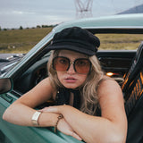 Person leaning out of a car window with sunglasses and a cap, with a scenic background wearing Soul Sister since 1969