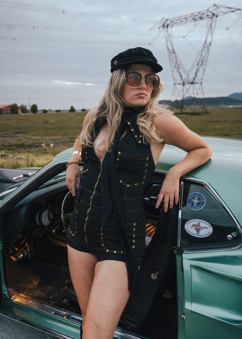 Woman in a black outfit and sunglasses leaning against a vintage car with power lines in the background wearing Soul Sister since 1969.