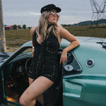 Woman in a black outfit leaning against a vintage green car in an open field wearing Soul Sister since 1969.