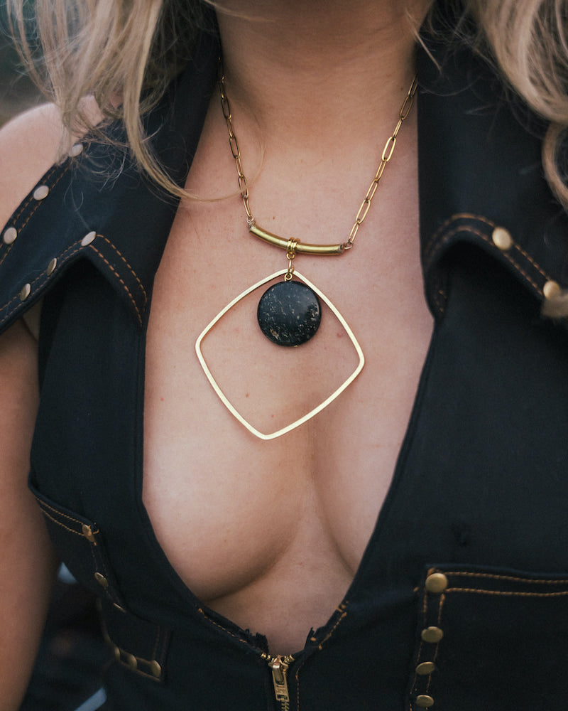 Person wearing a gold necklace with a black pendant, partially visible outfit