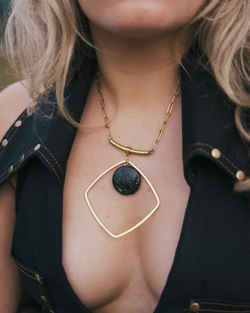 Gold necklace with a black pendant worn by a person