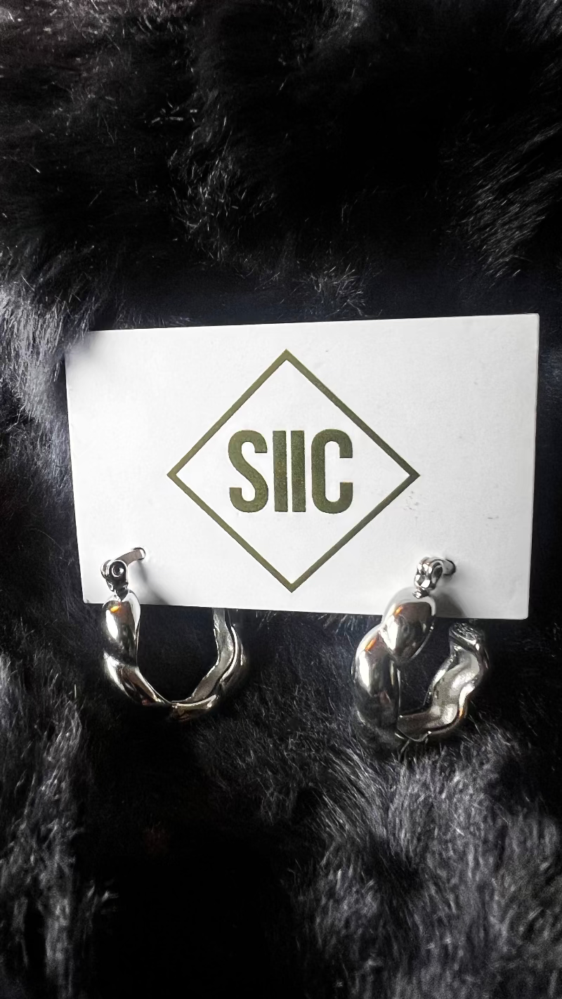 Pair of gold antler-shaped earrings on a card with 'SIIC' logo against a dark fur background