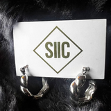 Pair of gold antler-shaped earrings on a card with 'SIIC' logo against a dark fur background