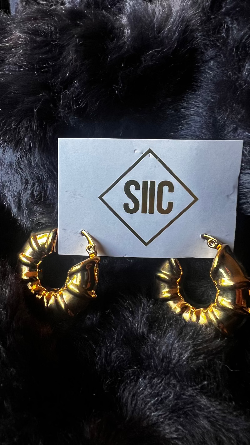 Gold hoop earrings on a card with 'SIIC' logo against a black fur background