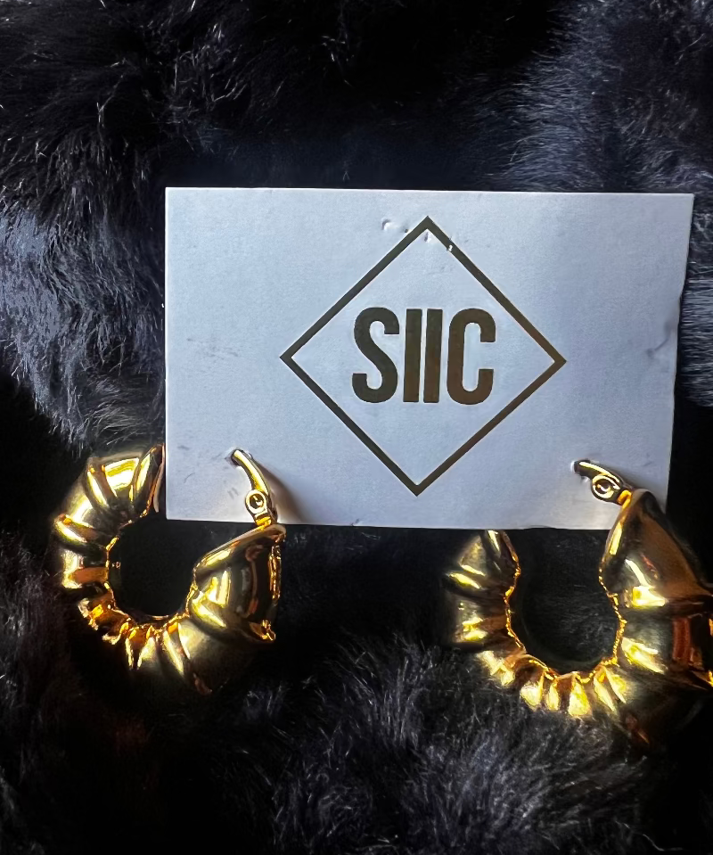 Gold hoop earrings on a card with 'SIIC' logo against a black fur background