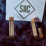 Gold earrings on a card with 'SIIC' logo on a dark fur background