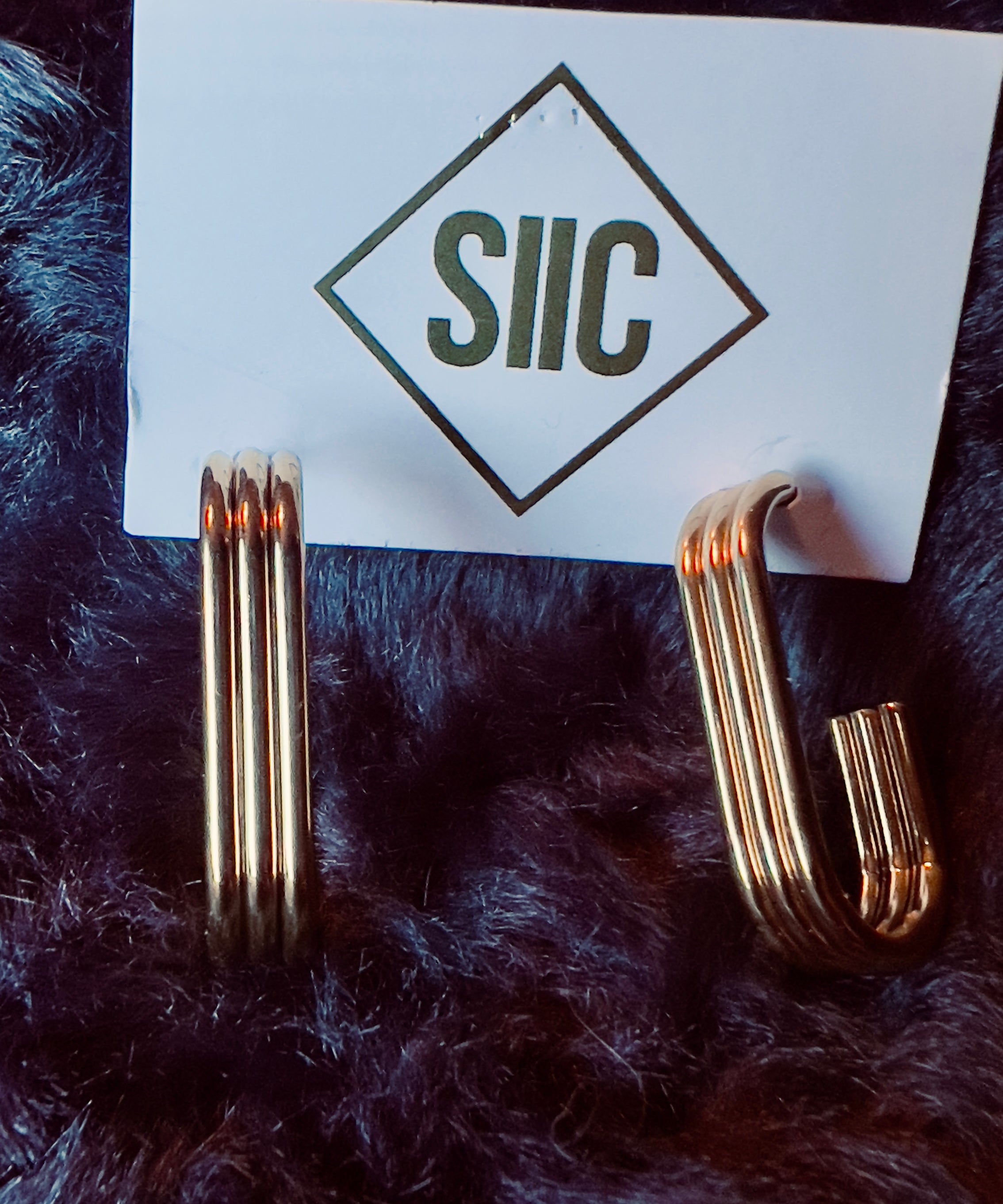 Gold earrings on a card with 'SIIC' logo on a dark fur background
