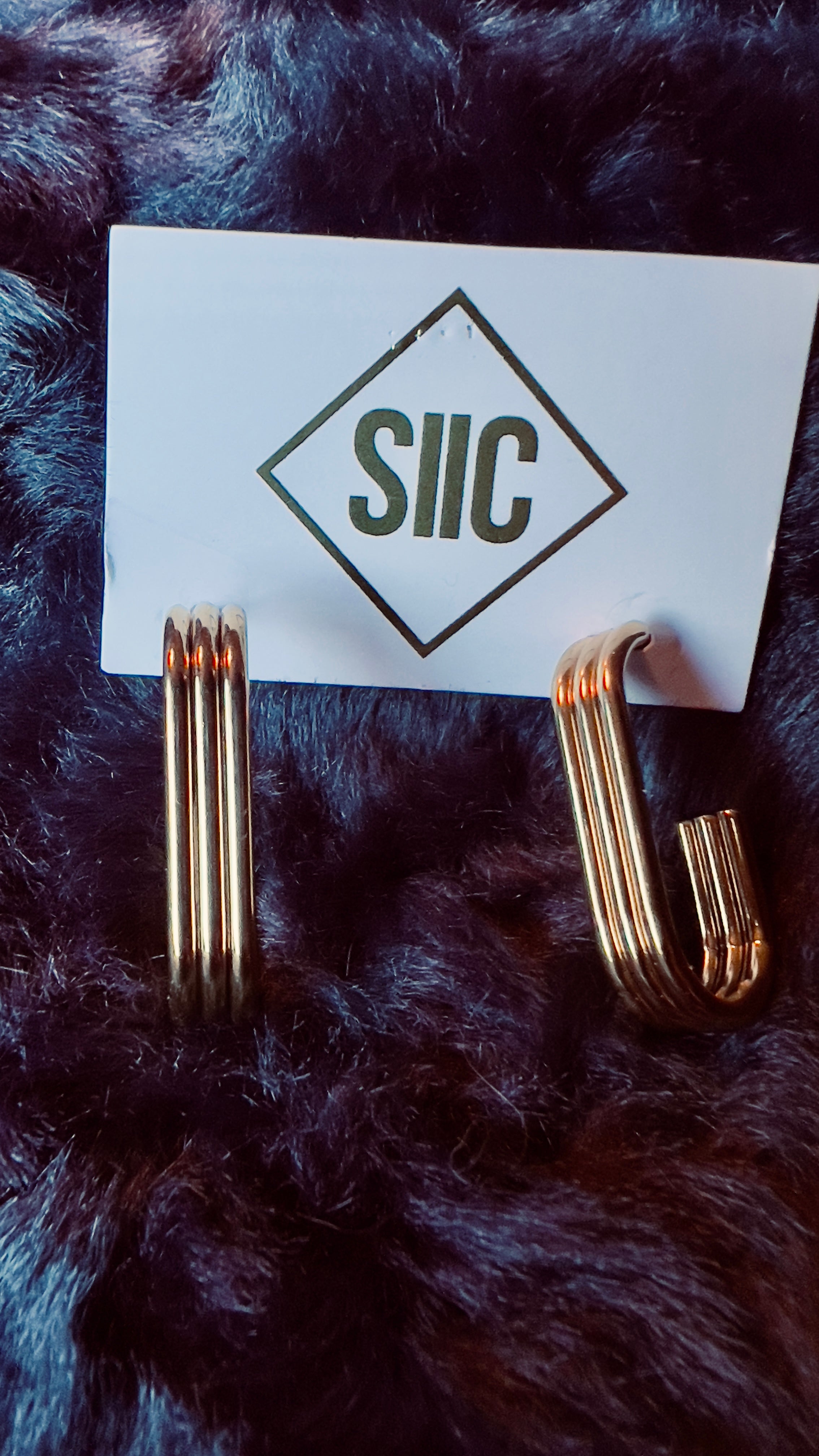 Gold earrings on a card with 'SIIC' logo on a dark fur background