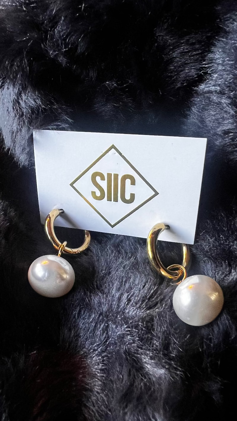 Pearl earrings on a card with 'SIC' logo against a dark fur background