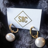 Pearl earrings on a card with 'SIC' logo against a dark fur background