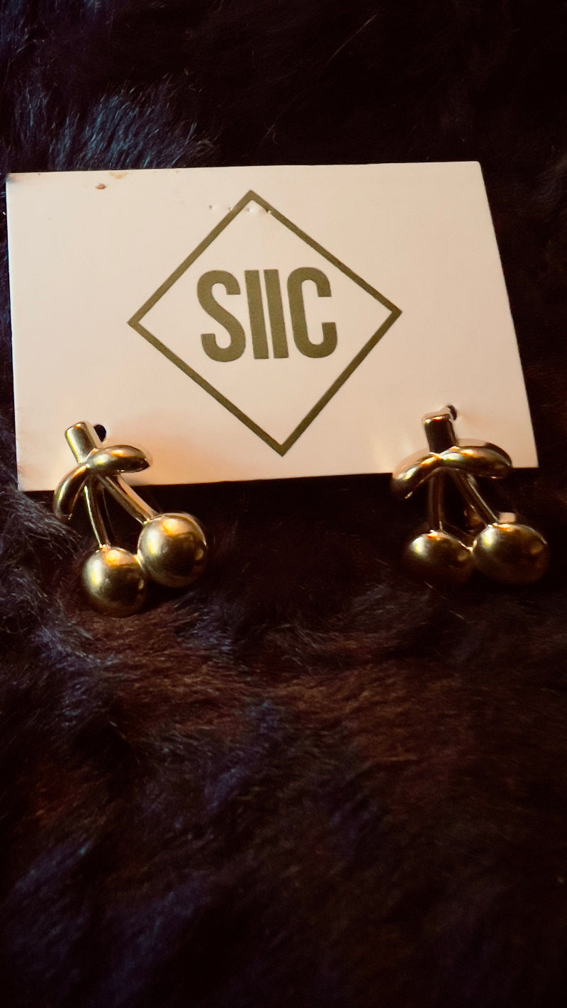 Gold earrings on a card with 'SIIC' logo on a dark fur background