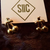 Gold earrings on a card with 'SIIC' logo on a dark fur background