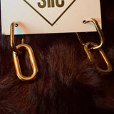 Gold chain-link earrings on a card with 'SIIC' branding against a dark background