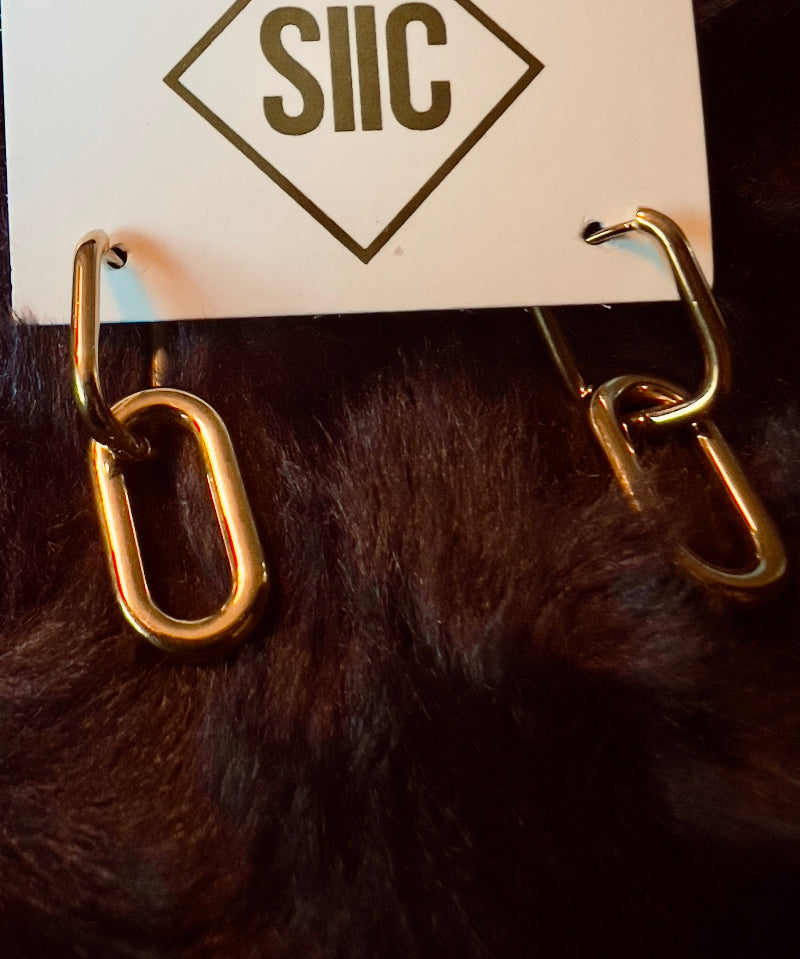 Gold chain-link earrings on a card with 'SIIC' branding against a dark background