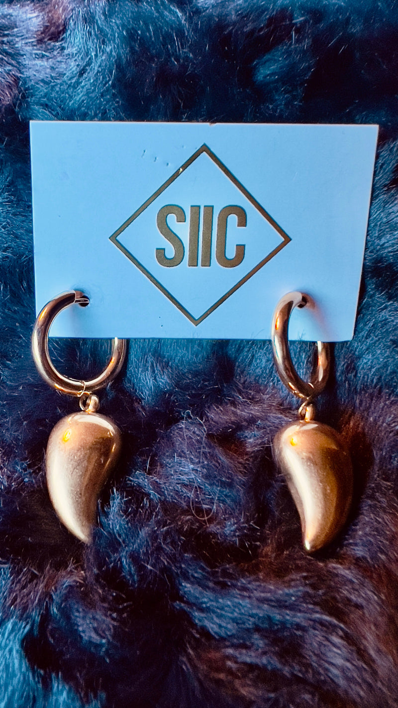 Gold spike earrings on a blue card with 'SIIC' branding against a dark fur background