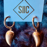 Gold spike earrings on a blue card with 'SIIC' branding against a dark fur background