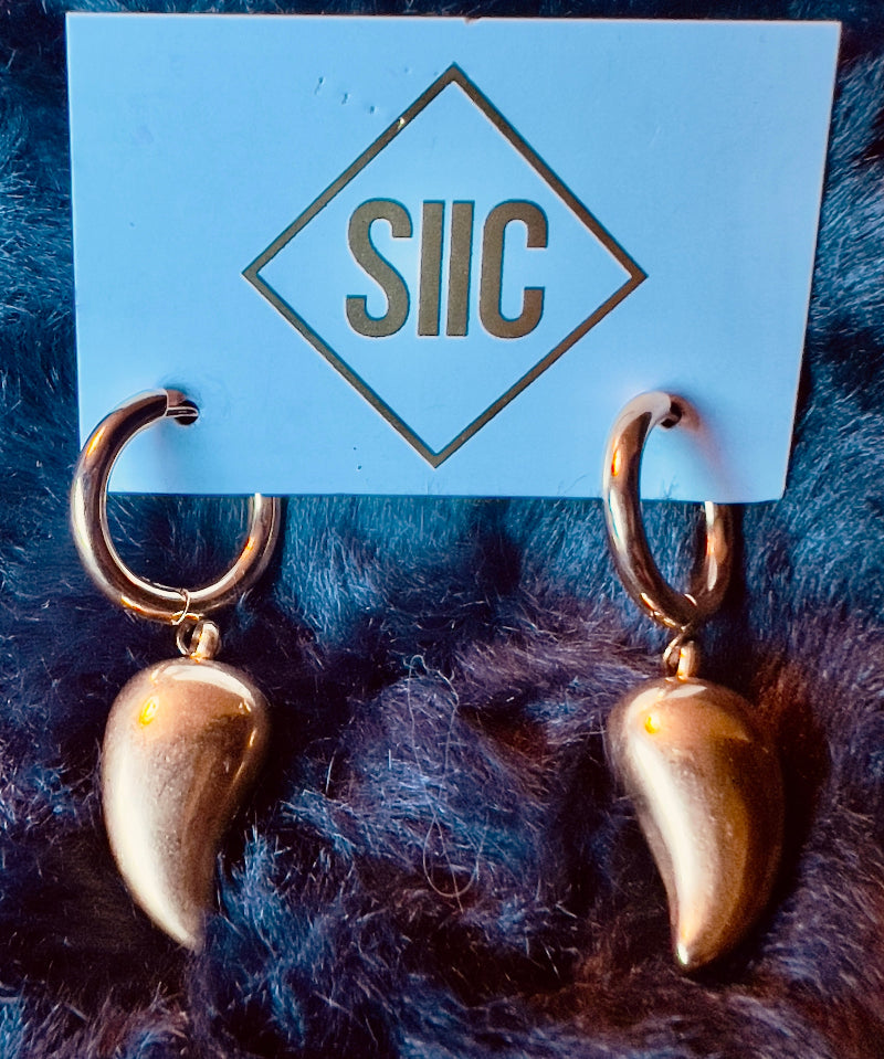 Gold spike earrings on a blue card with 'SIIC' branding against a dark fur background