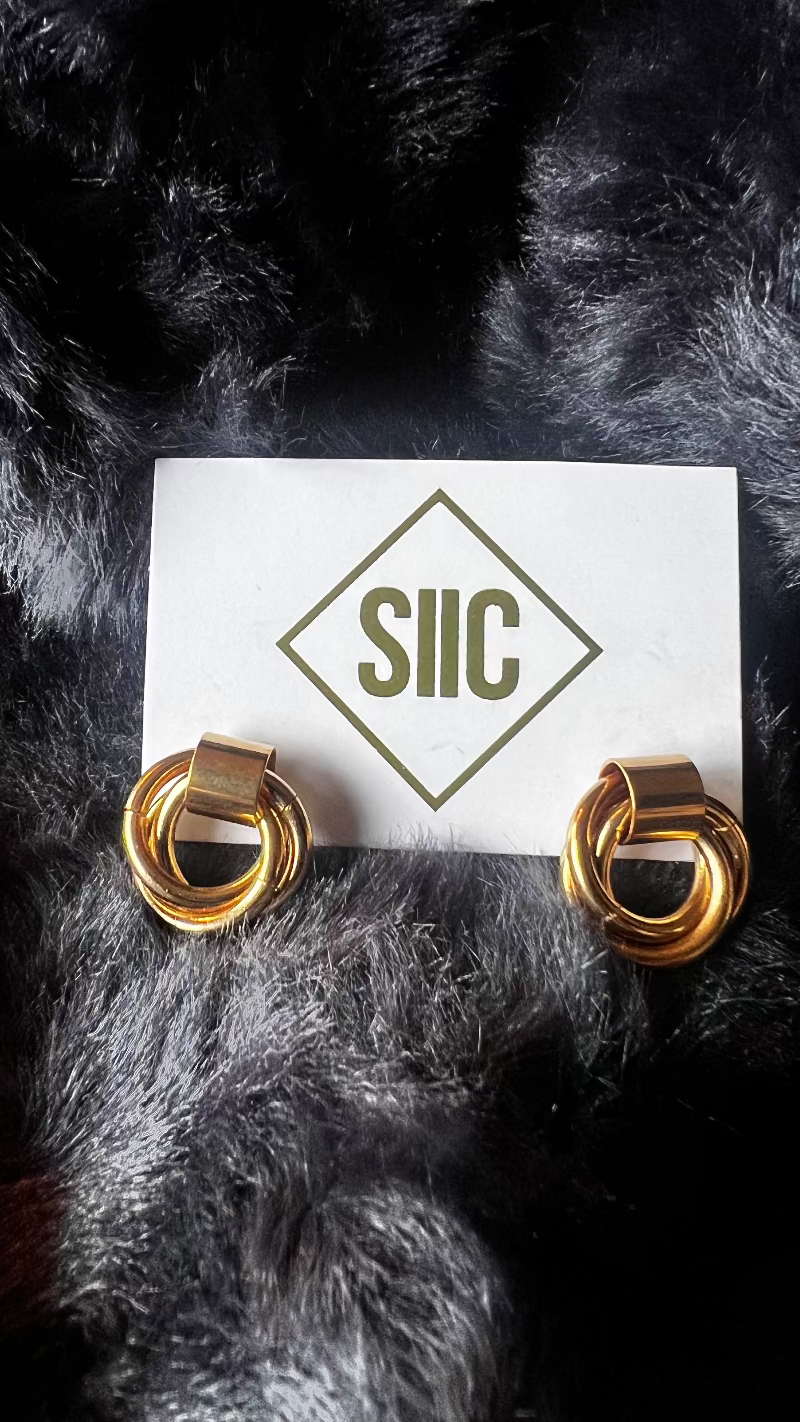 Gold hoop earrings on a card with 'SIIC' logo against a dark fur background
