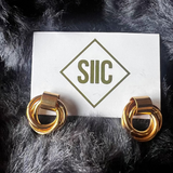 Gold hoop earrings on a card with 'SIIC' logo against a dark fur background
