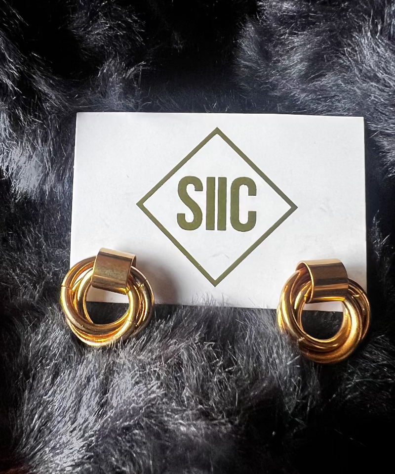 Gold hoop earrings on a card with 'SIIC' logo against a dark fur background