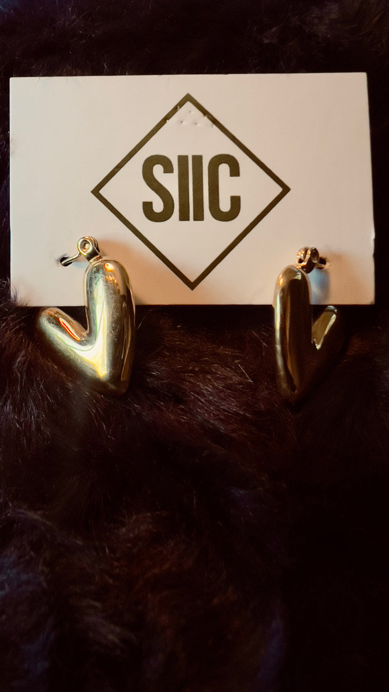 Gold heart-shaped earrings on a card with 'SIIC' logo against a dark background