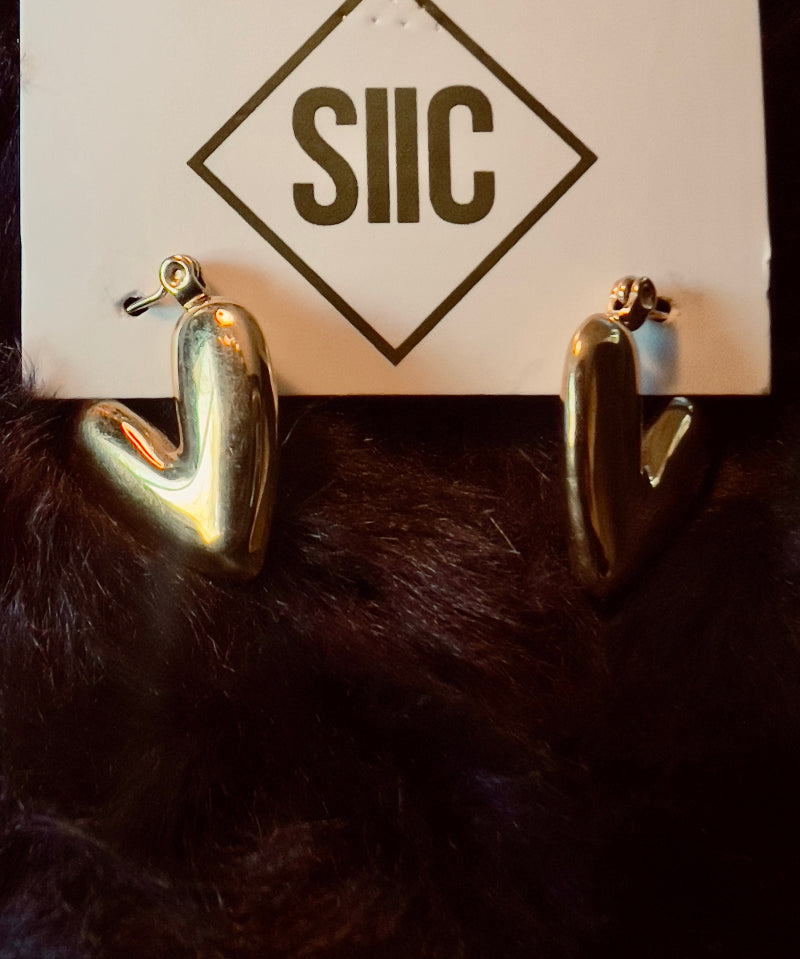 Gold heart-shaped earrings on a card with 'SIIC' logo against a dark background
