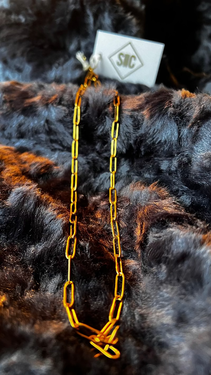 Gold chain necklace on a dark fur background with a visible brand tag.
