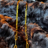 Gold chain necklace on a dark fur background with a visible brand tag.